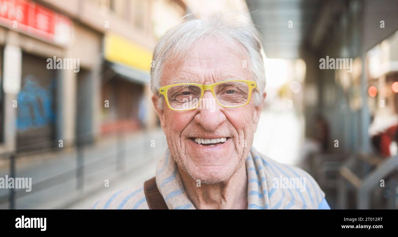 Senior man smiling in front of camera while waiting tram at city station - Citizen lifestyle and transportation concept - Focus on mouth Stock Photo