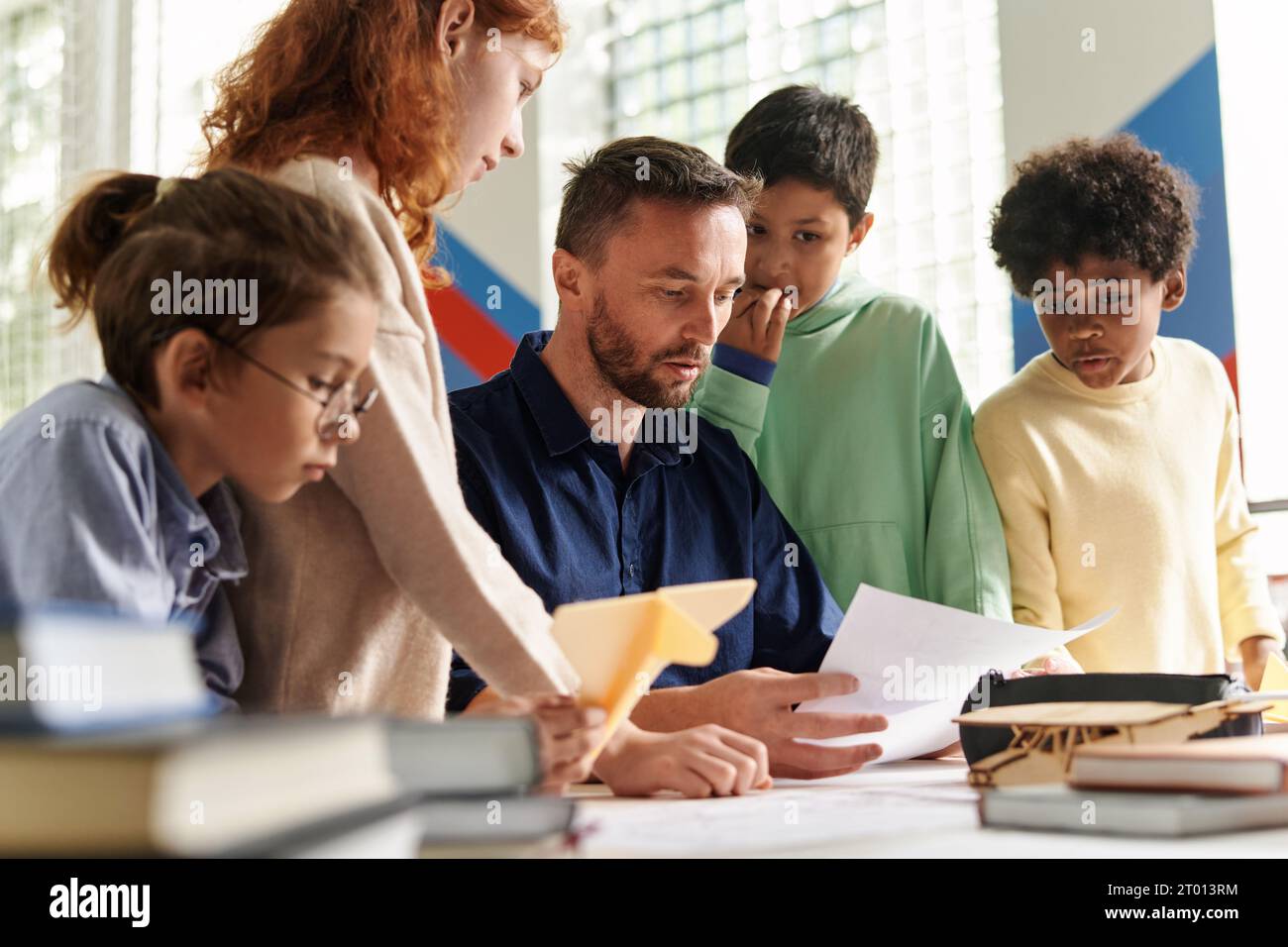 Kids gathered at desk of aeromodeling class teacher checking ...