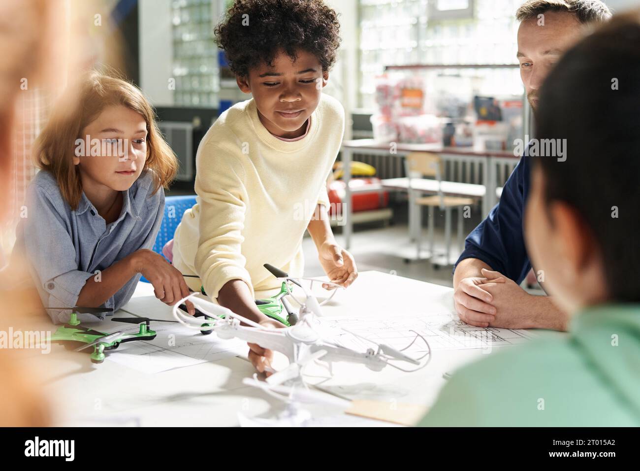 Curious kid taking quadcopter from table when attending aeromodeling class Stock Photo