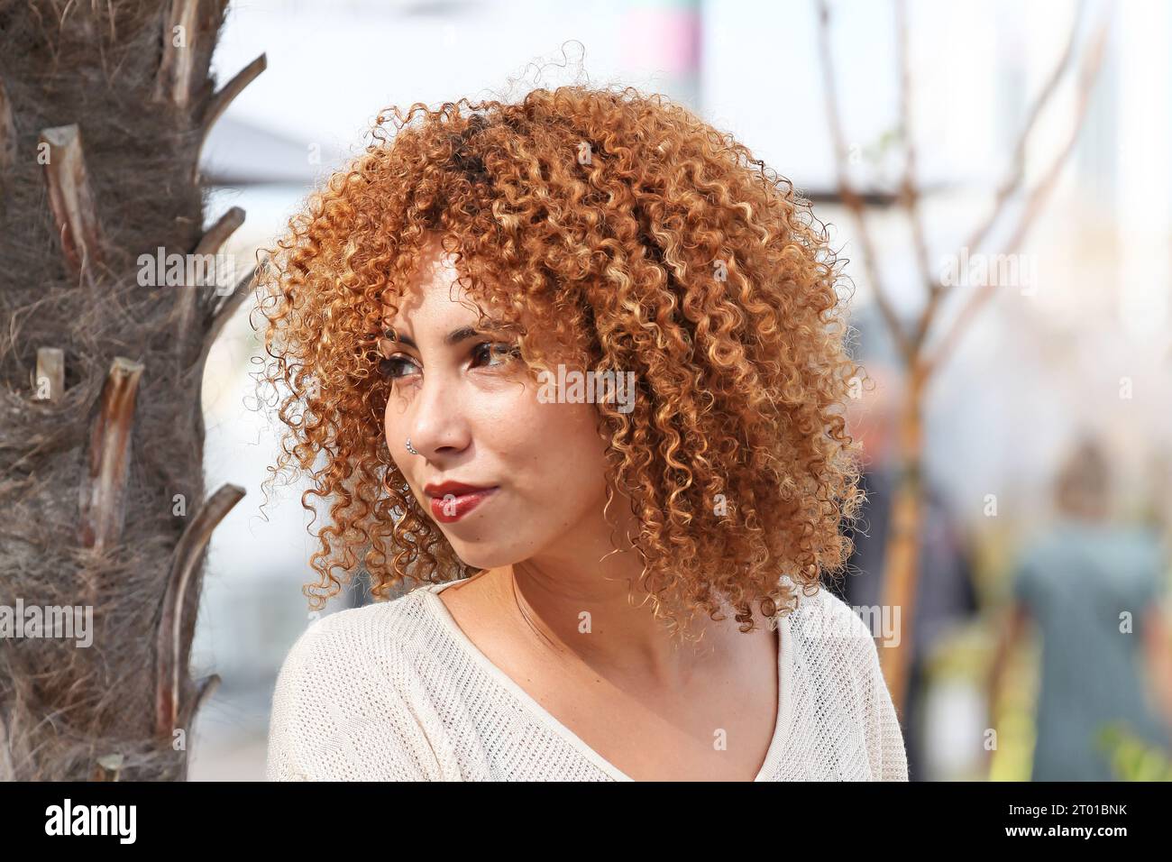 Curly hair woman in white sweater and red pants having a good time outside under a palmer tree in a tropical country Stock Photo