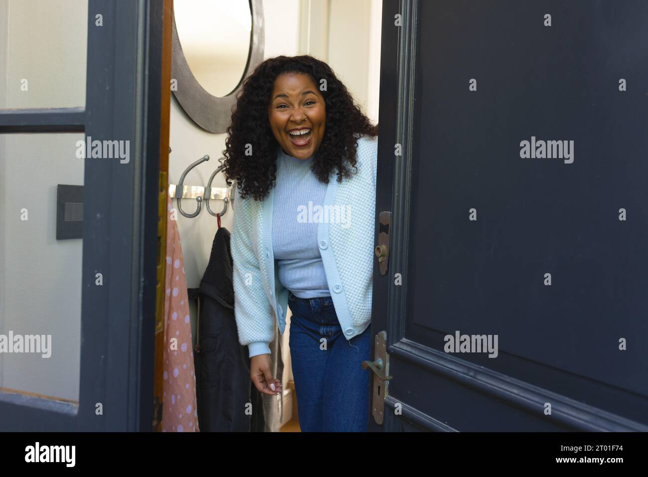 Happy african american woman opening door and laughing in sunny house Stock Photo