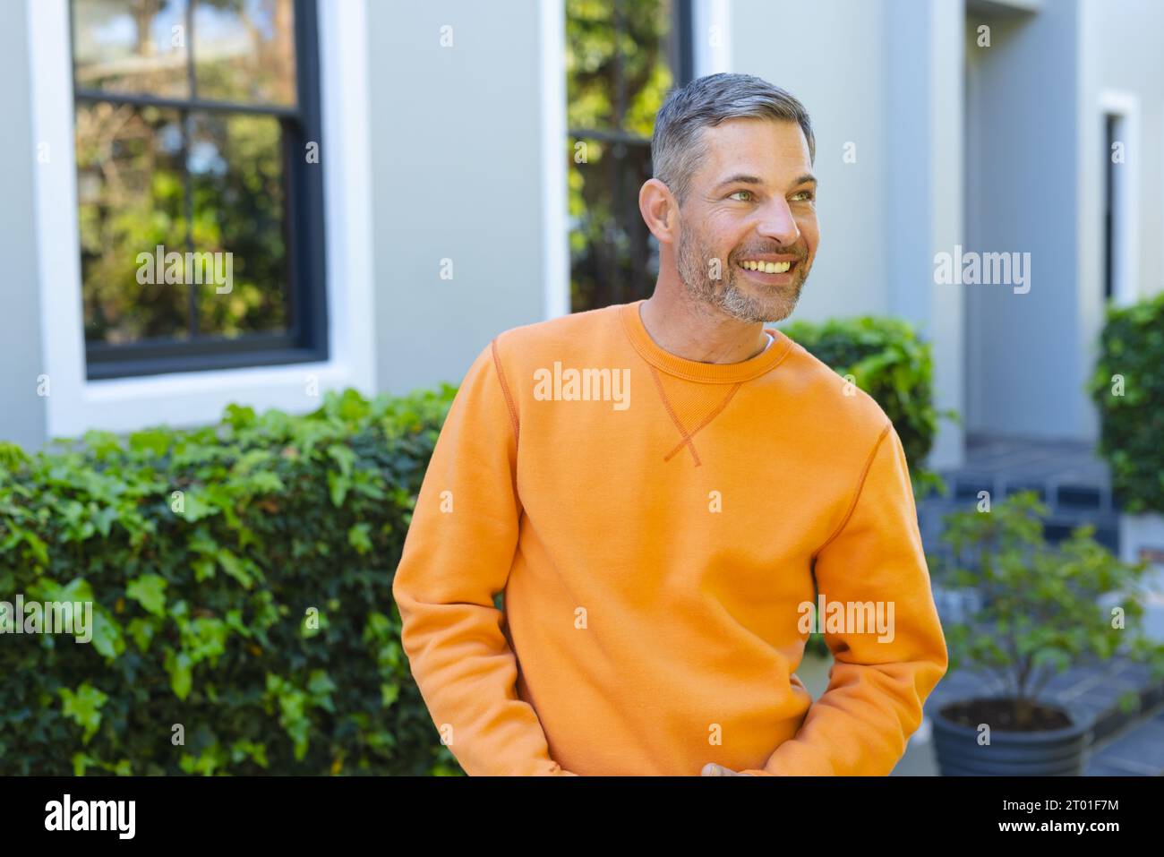 Happy caucasian man standing and smiling in front of house in sunny garden Stock Photo