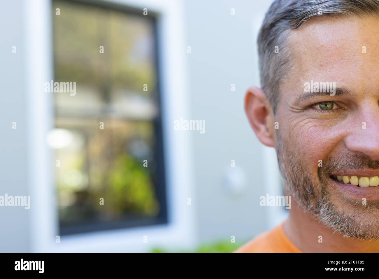 Half face of happy caucasian man standing and smiling in front of house in sunny garden Stock Photo
