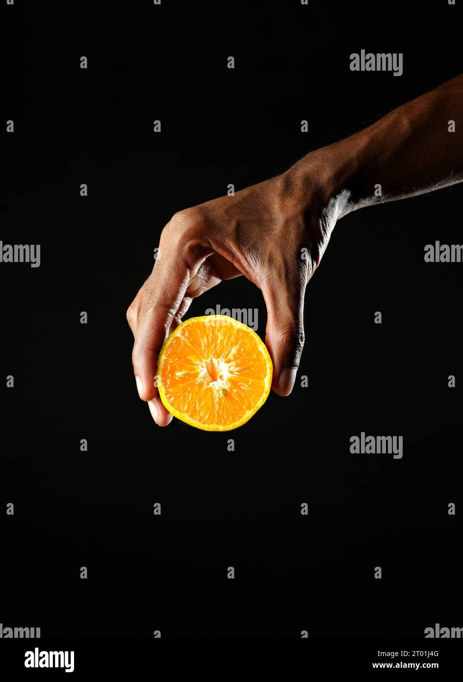Man holding a section of orange and squeezing it, black background, sharp image Stock Photo