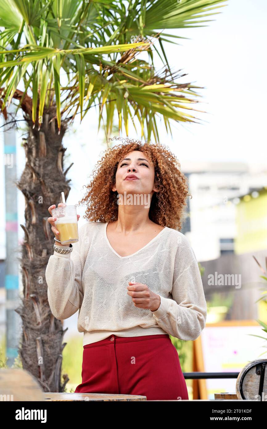 Curly hair woman in white sweater and red pants having a good time outside under a palmer tree in a tropical country Stock Photo