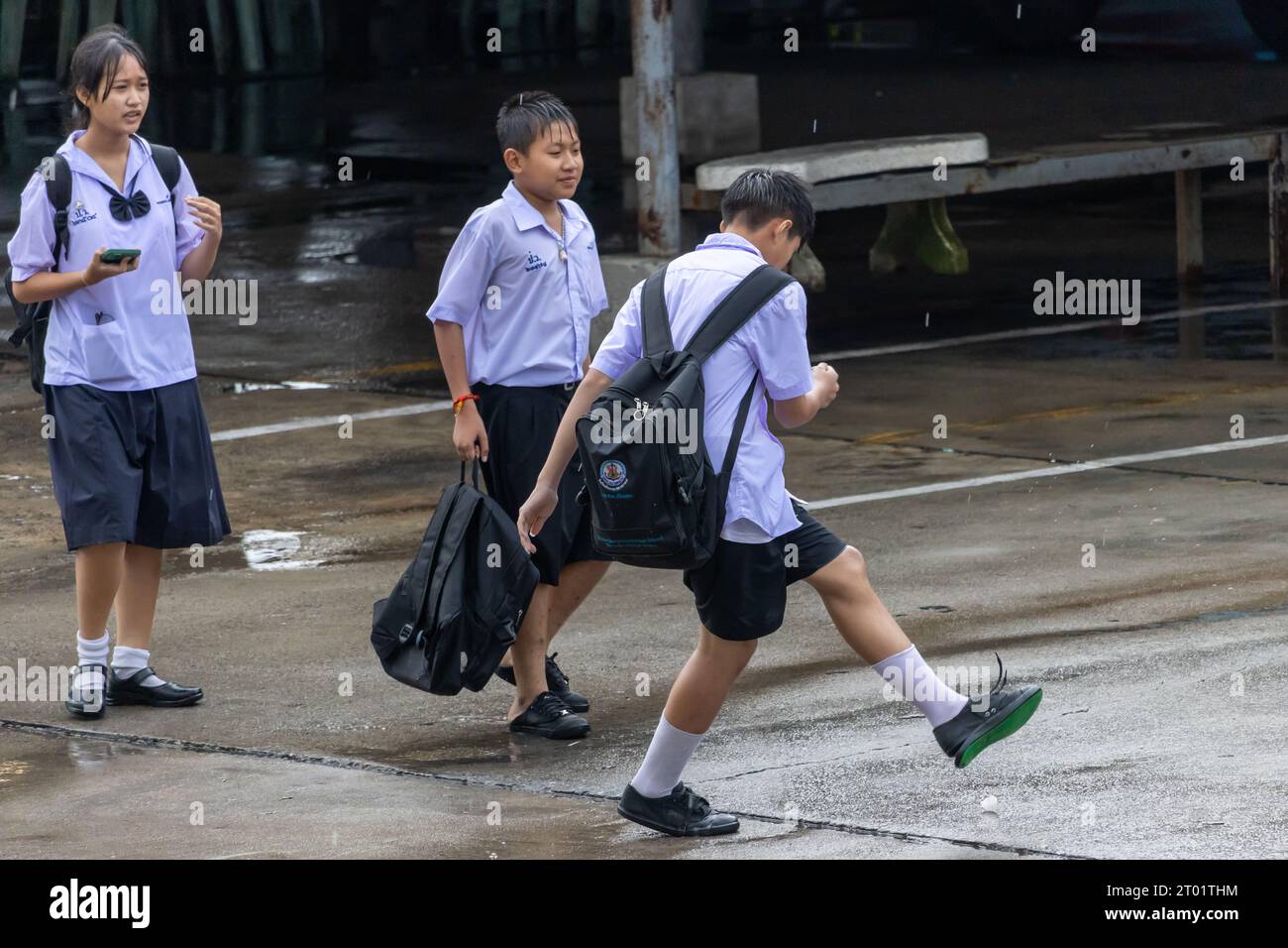 SAMUT PRAKAN, THAILAND, SEP 20 2023, Cheerful schoolchildren in uniforms play games on the rainy street Stock Photo