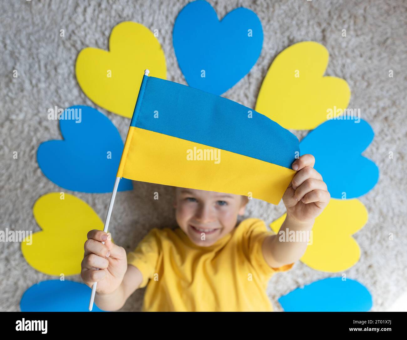 The child's hands hold the Ukrainian flag. the child lies among blue and yellow hearts. Independence Day. Love Ukraine, patriotism, peace and the anti Stock Photo
