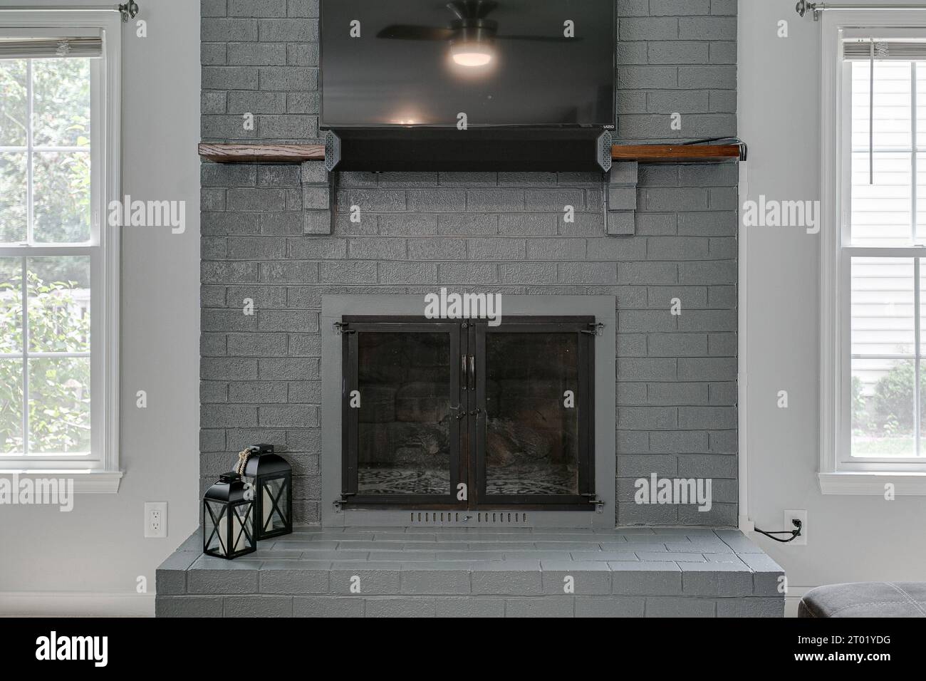 Grey Brick Fireplace with TV Hung on Wall and Two Candle Light Farmhouse Lanterns and Sunny Windows Stock Photo