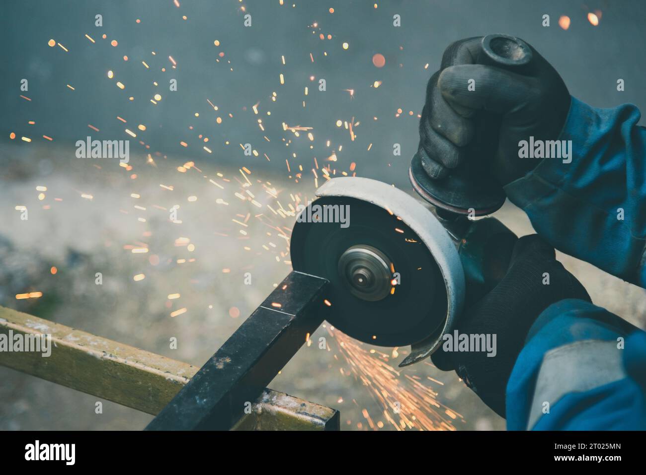 Man wearing safety gloves is cutting a metal with hand grinder machine. Lots of sparks. Stock Photo
