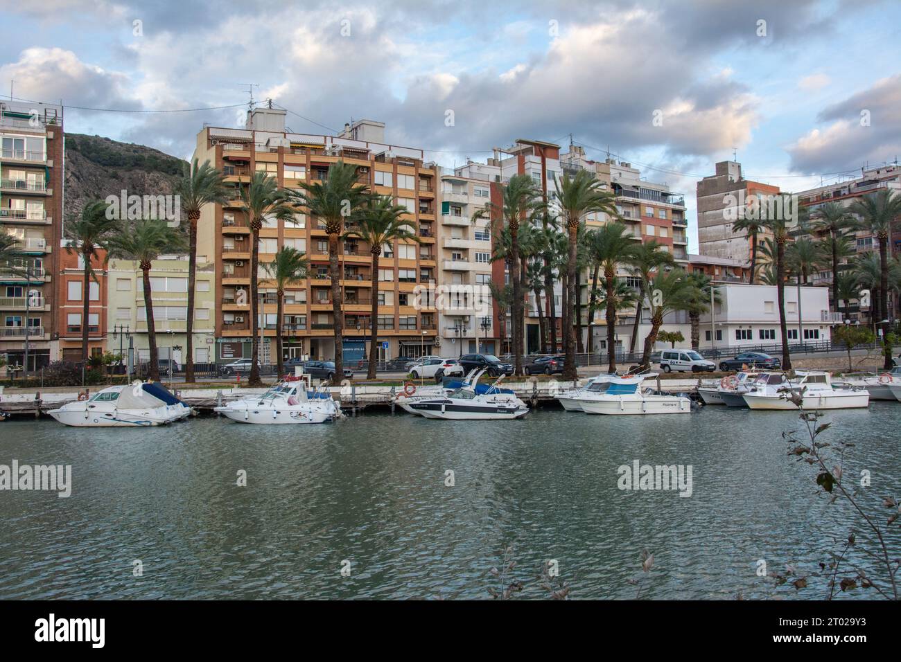 Cullera, Spain – January 8, 2023 -  View across the Jucar river with residential buildings, boats and palm trees in Cullera city in Spain Stock Photo