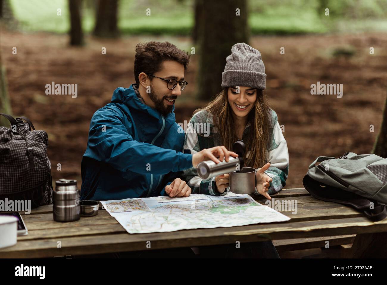 Positive young caucasian family in jackets sit at table, drinking coffee, look at route map, enjoy adventure Stock Photo