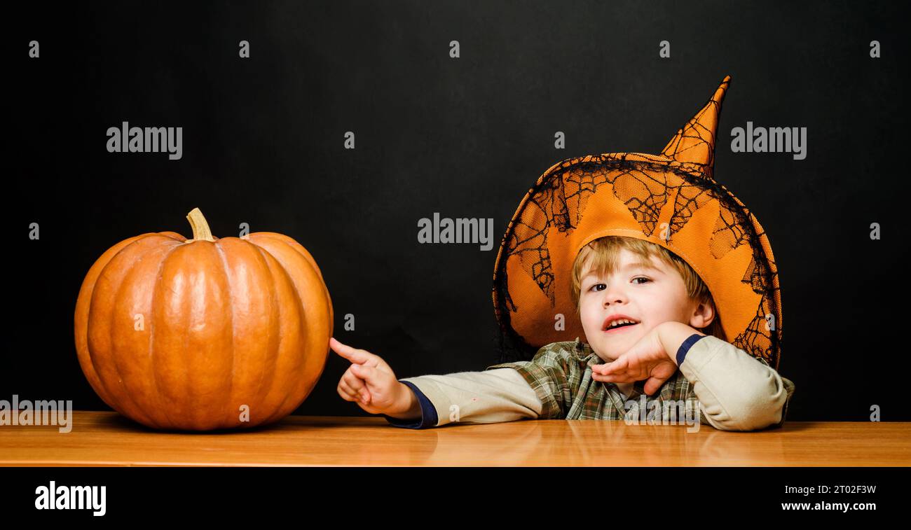 Halloween. Little boy in witch hat with pumpkin. Halloween kid with jack-o-lantern. Trick or treat. Little child wizard, magician prepares for Stock Photo