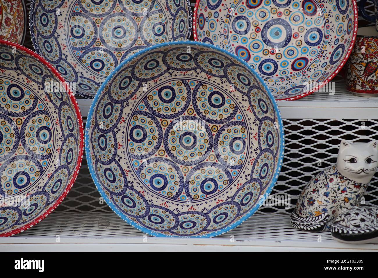 Rows of beautiful multi coloured decorative Bowls, Various Holders and Cats on White Mesh Shelves with Evil Eye and Floral Designs facing forward. Stock Photo