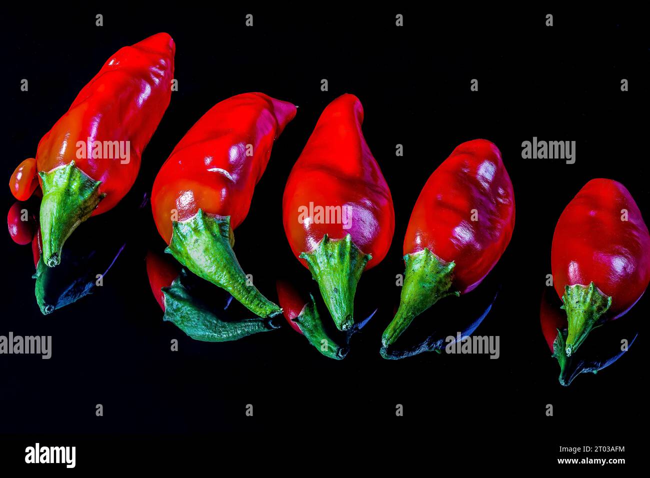 Five ripe red chili peppers isolated on a black reflecting background Stock Photo