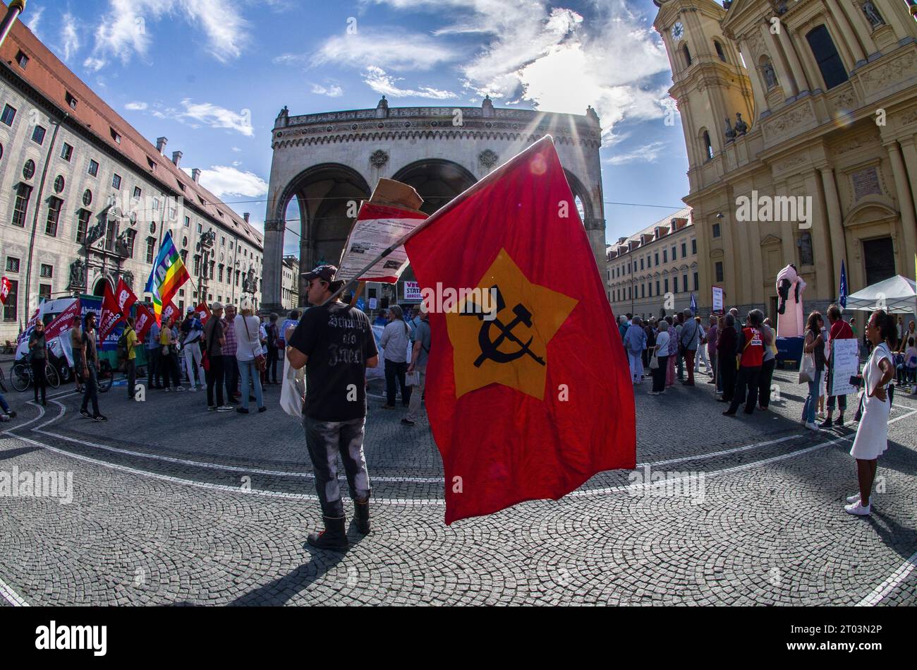 Munich, Bavaria, Germany. 3rd Oct, 2023. A demonstrator against the support of Ukraine holds a form of a Soviet flag with a gun on it in front of the Feldherrnhalle. The Linkes Buendnis gegen Krieg demonstrating at Odeonsplatz while its far-rght partner Muenchen Steht Auf was at Marienplatz. On the Day of German Unity (Tag der Deutschen Einheit), the pro-Russia Muenchen Steht Auf conspiracy extremist group and their associates organized a protest against Germany's support for Ukraine while the associated Friedensbuendnis organized another demo at Odeonsplatz. The MSA group is a combination Stock Photo