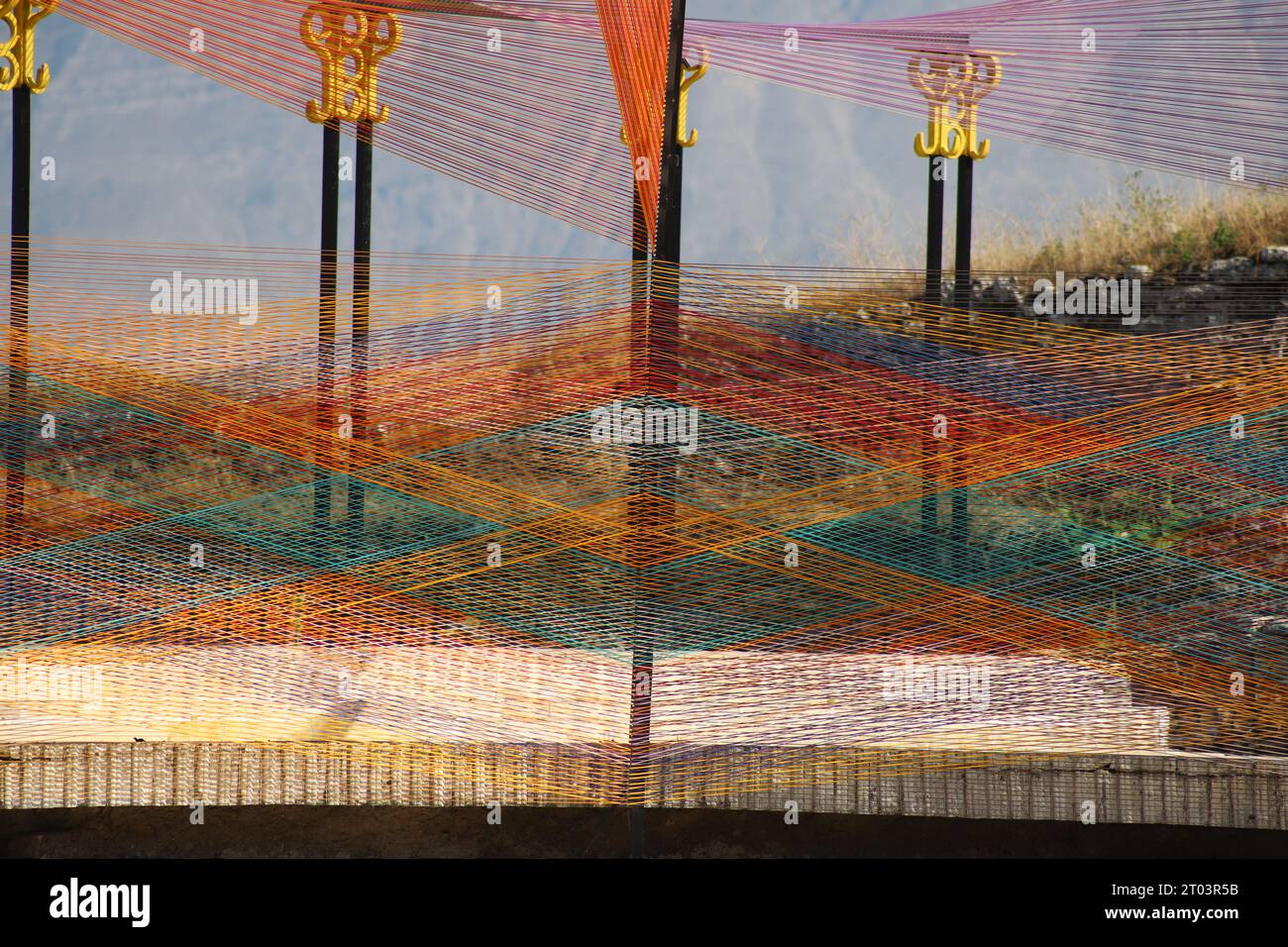 An Aesthetically pleasing, Modern Art Design Outdoor Stage, made of multiple multicoloured interwoven String, Cord or Twine with a Mountain backdrop. Stock Photo