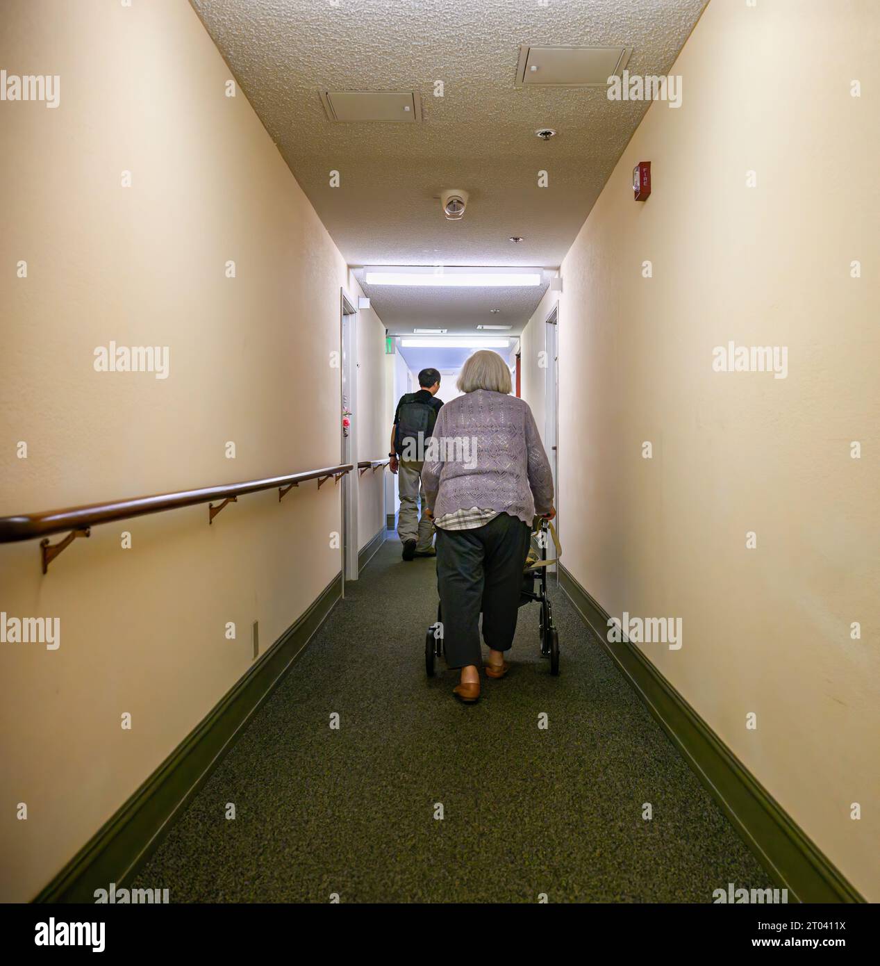 Senior woman walking using a mobility walker in the apartment corridor. Vertical format. Stock Photo