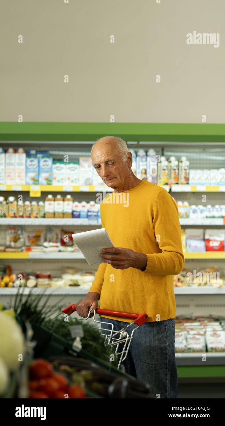 Elderly man at the supermarket shopping with a grocery list and pushing ...