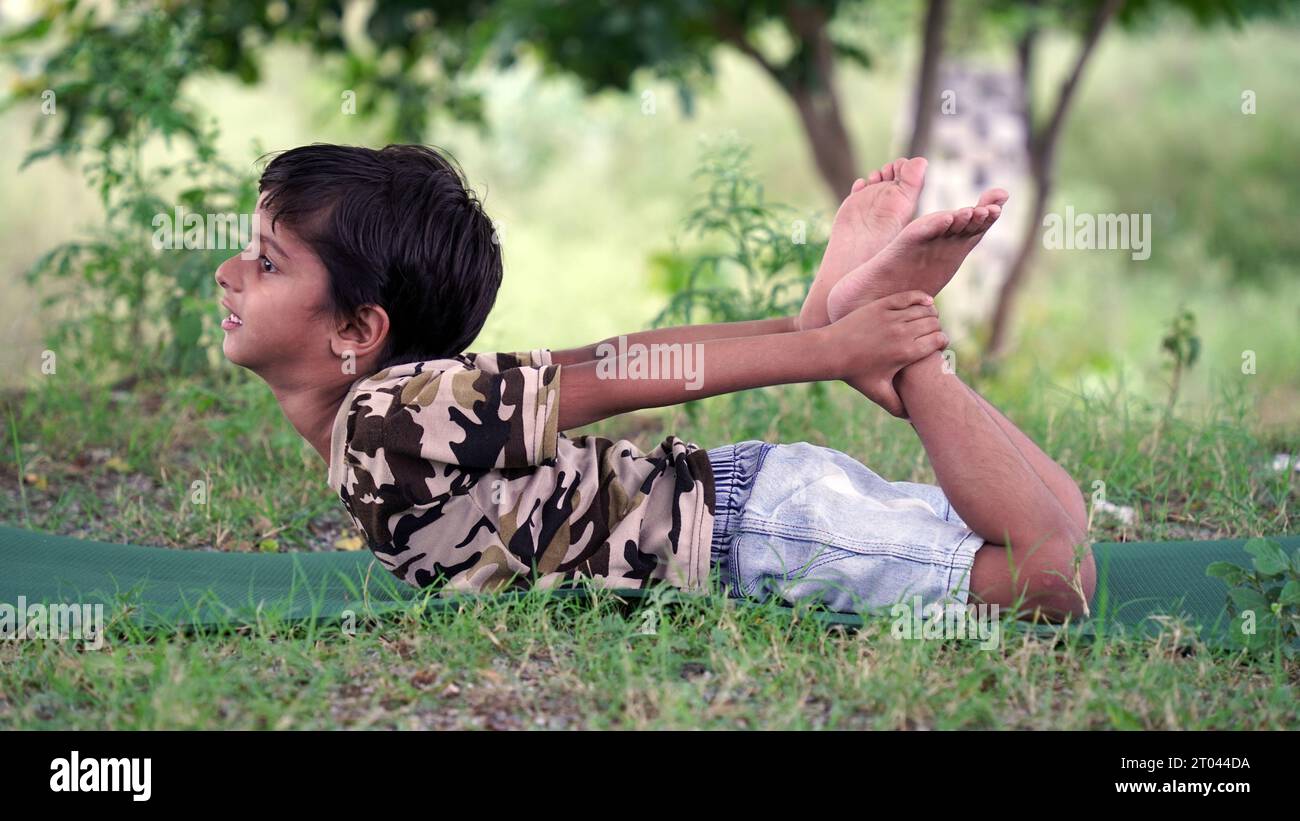 Portrait of gorgeous kid practicing yoga outdoor. Beautiful child practice yoga asana or doing gymnastic exercises. Little kids meditating in lotus po Stock Photo