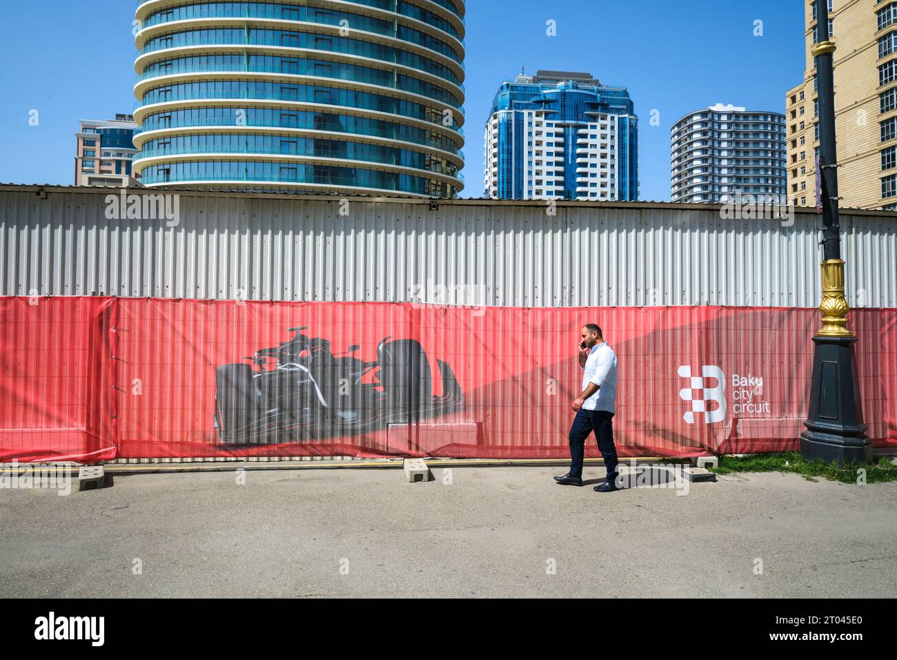 A man walks along temporary fencing with large, red race car graphic. At the Formula 1, Formula One race track prep area in Baku, Azerbaijan. Stock Photo