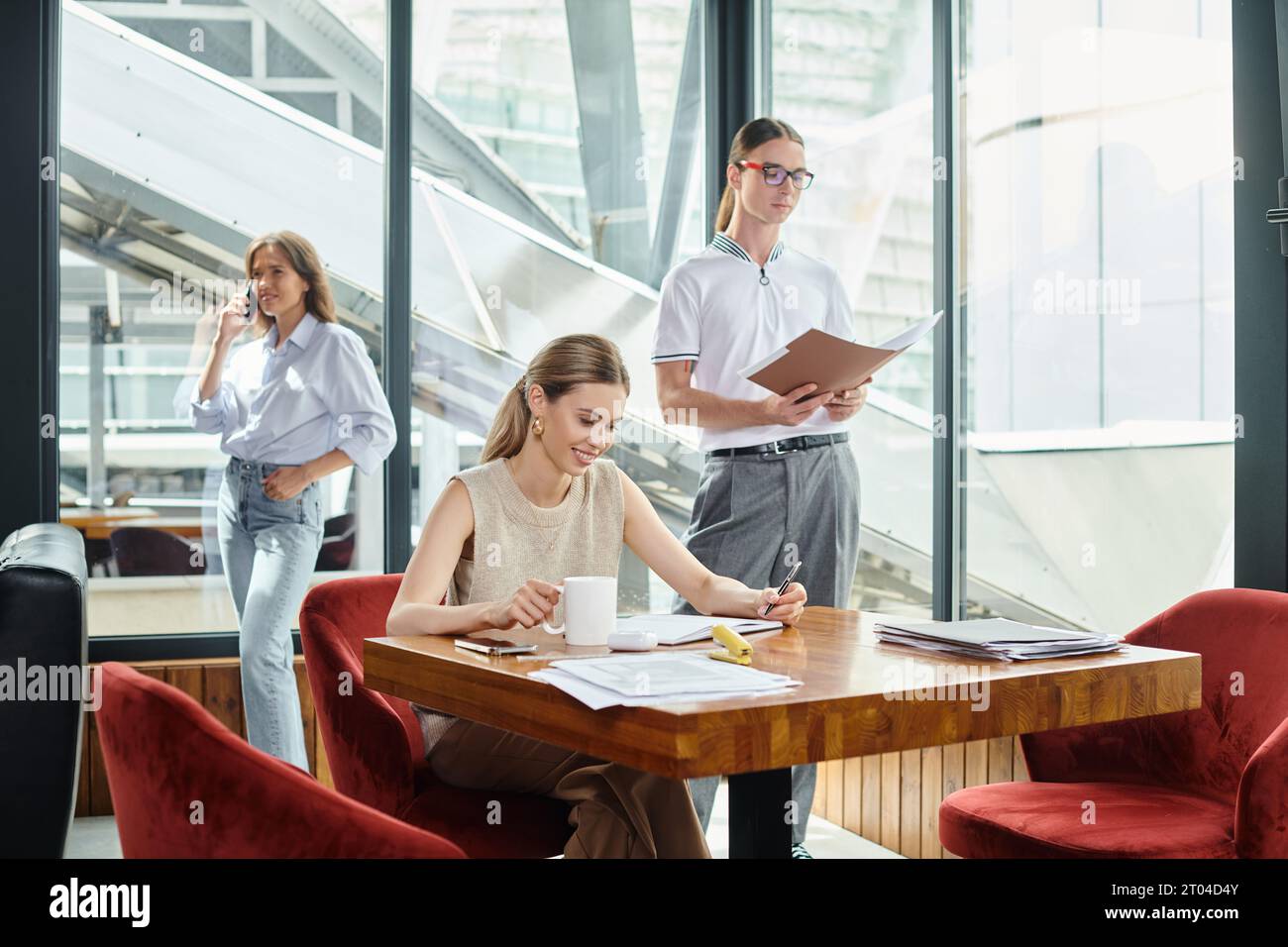 two young colleagues in smart wear working on their papers and one talking on phone, coworking Stock Photo