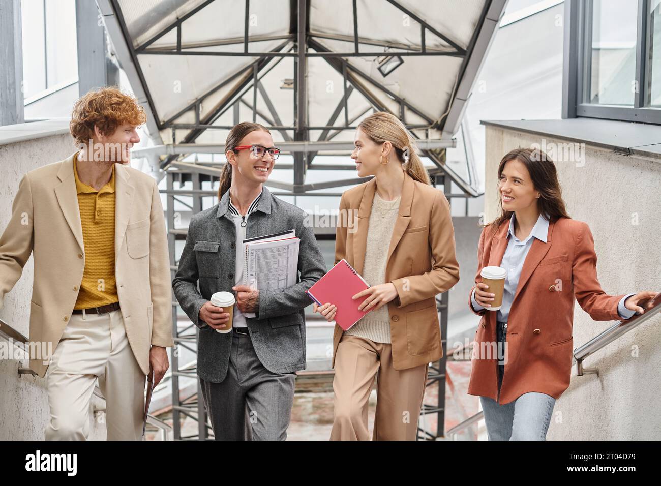 four colleagues smiling sincerely at each other holding coffee and paperwork in hands, coworking Stock Photo