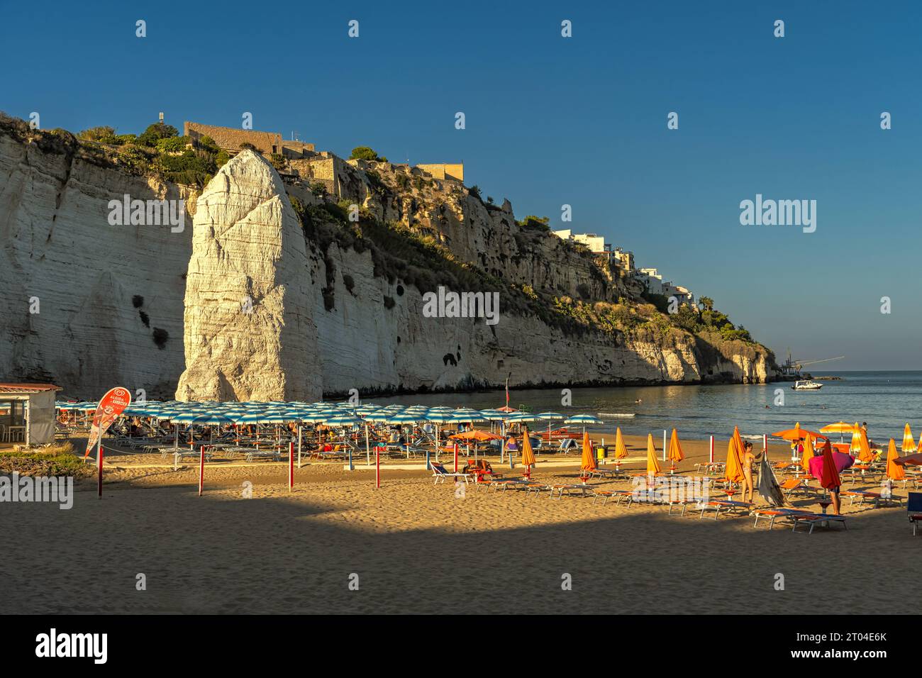 The sandy beach of Pizzomunno with the famous sea stack and the beach full of umbrellas on a hot late summer day. Vieste, Province of Foggia, Puglia Stock Photo