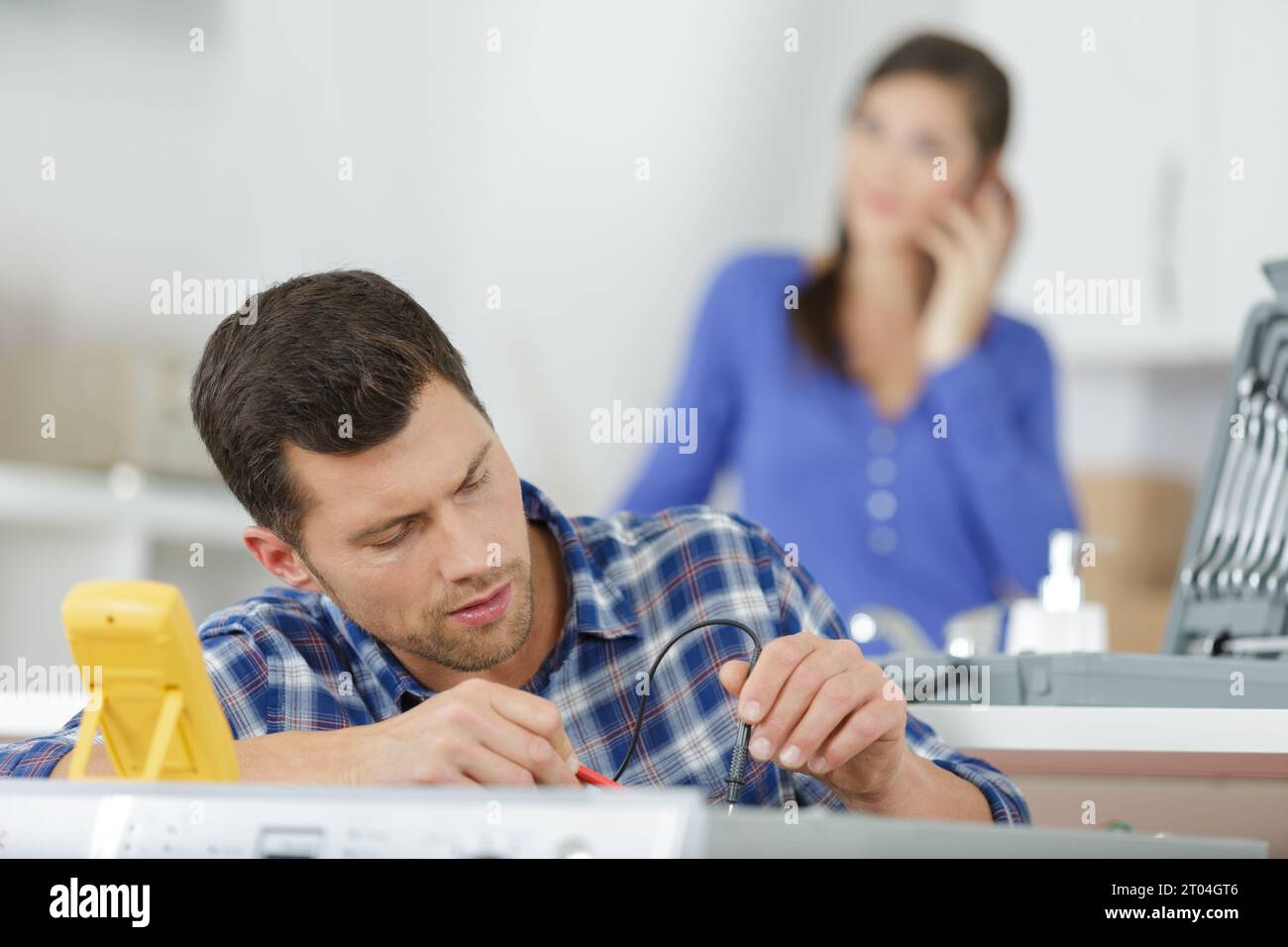 serviceman testing appliance with multimeter housewife in background Stock Photo
