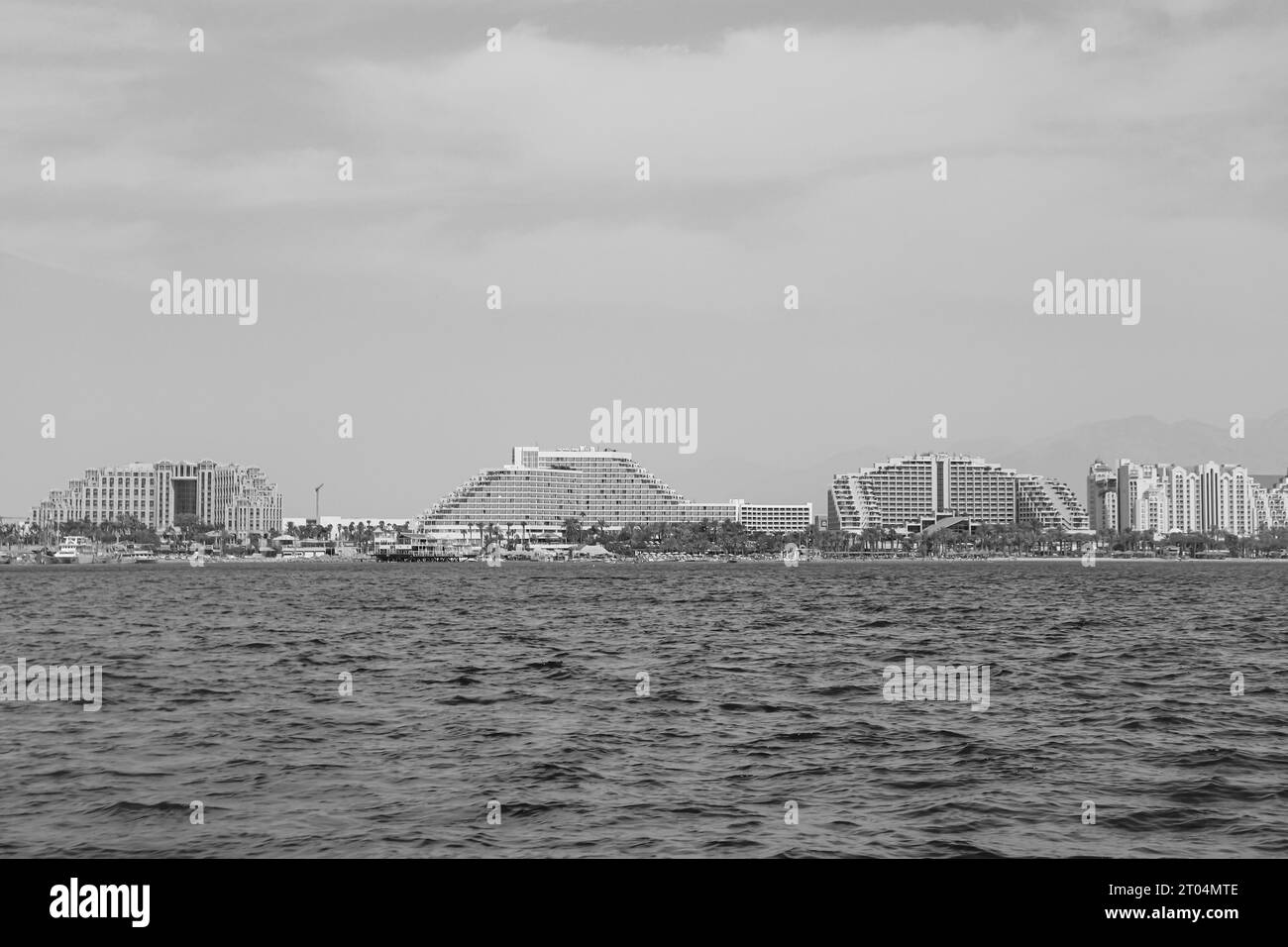 Boat view of Eilat harbour boardwalk luxury hotel resorts. (left to right) Queen Of Sheba, Royal Beach, Dan Eilat, Herods Palace in black and white Stock Photo