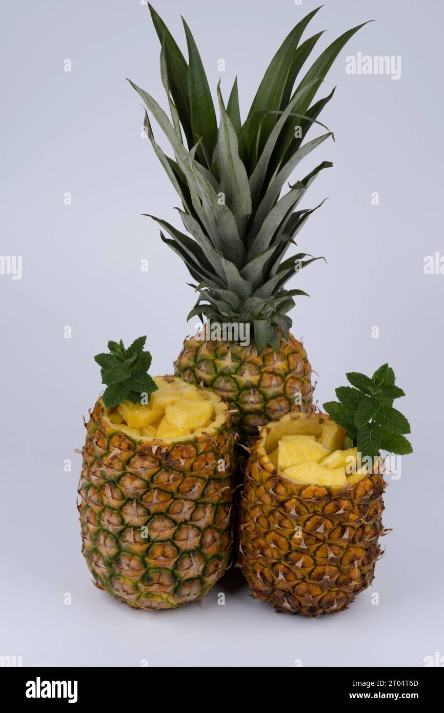 fresh pineapple, one whole fruit and two hollowed out fruit, filled with pieces of fruit pulp. set against white background Stock Photo