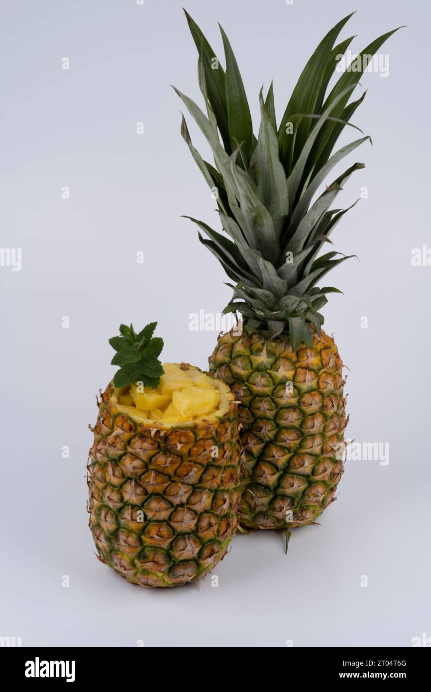fresh pineapple, one whole fruit and one hollowed out fruit, filled with pieces of fruit pulp. set against white background Stock Photo