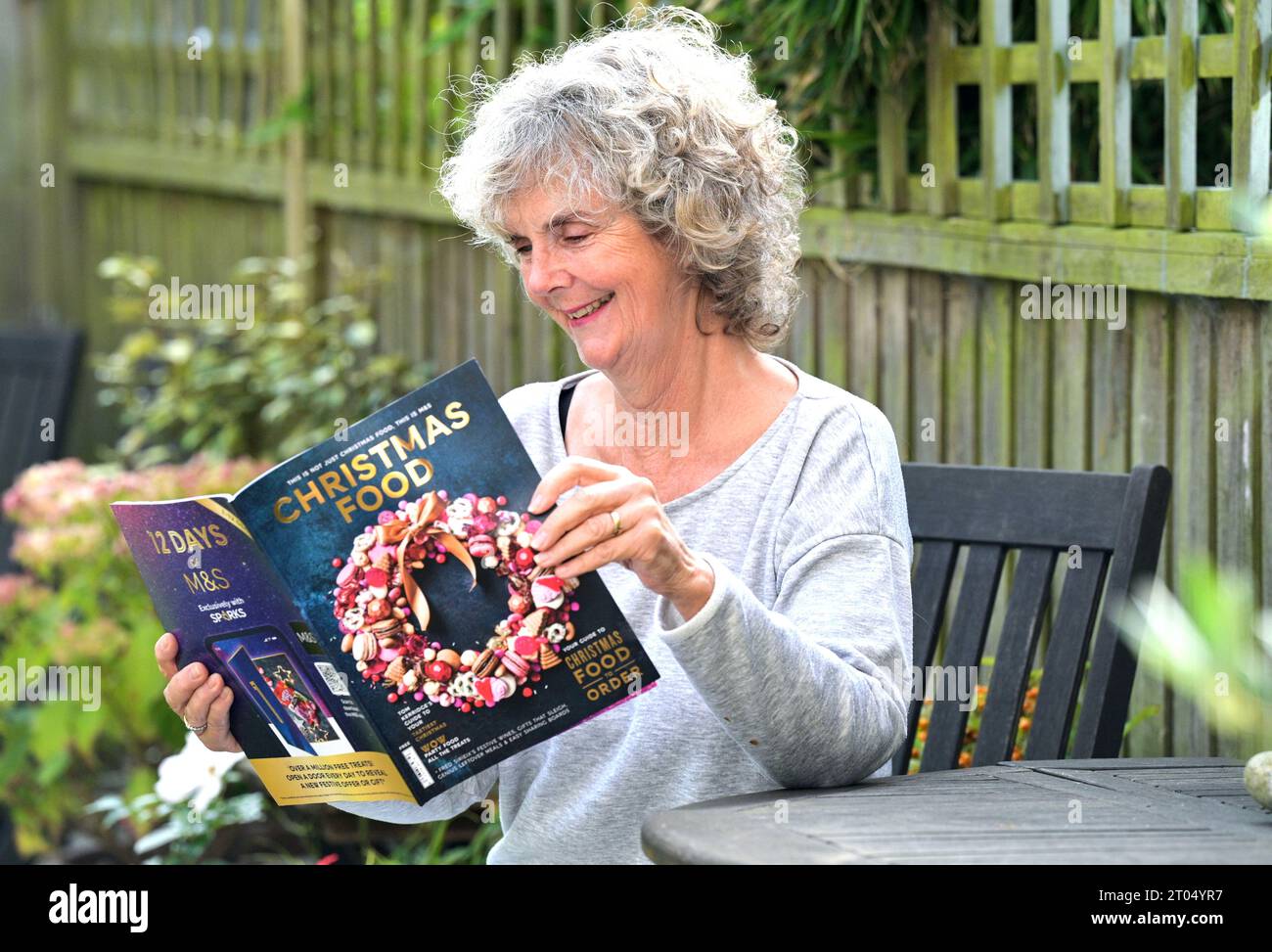 Woman reading the Marks & Spencer ( M&S) Christmas food ordering catalogue 2023 in her garden at home Stock Photo