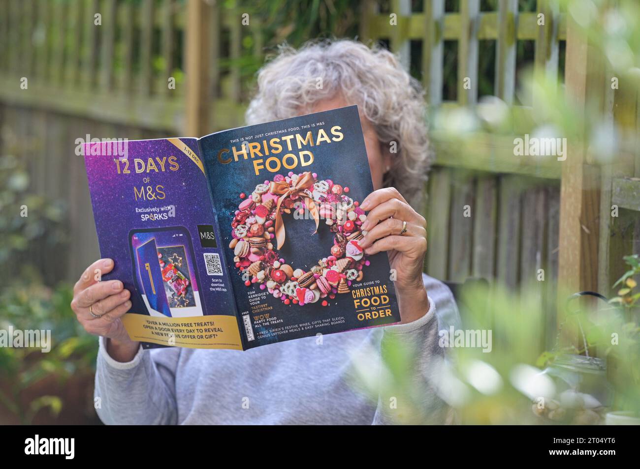 Woman reading the Marks & Spencer ( M&S) Christmas food ordering catalogue 2023 in her garden at home Stock Photo