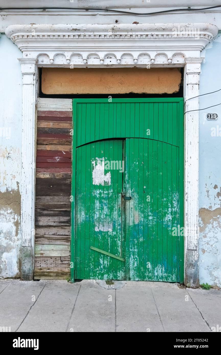Old wooden door with ancient carving decoration in the frame. The structure is surrounded by botched fixes. It is located in the Marta Abreu city stre Stock Photo
