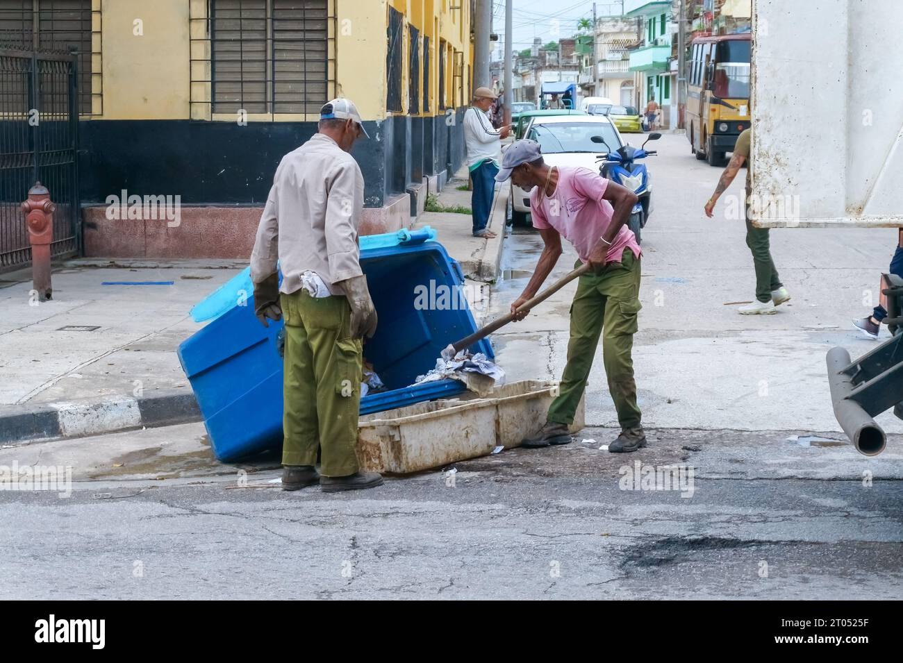 Cuban men working in garbage collection on a city street.They are emptying the large bin with a hoe while a truck is waiting for them.Santa Clara, Cub Stock Photo
