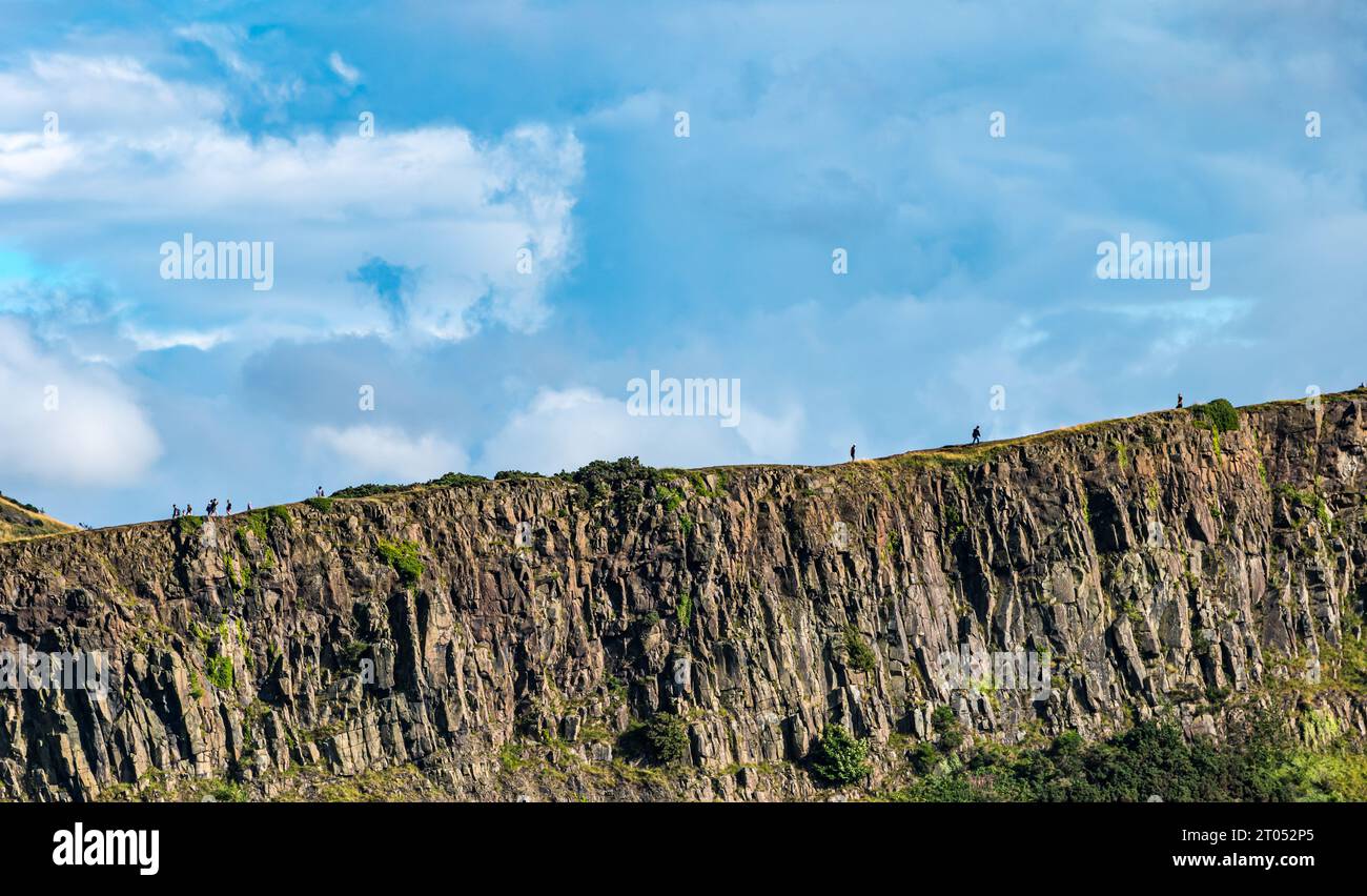 People walking on the cliff edge of rocky ledge of Salisbury Crags, Edinburgh, Scotland, UK Stock Photo
