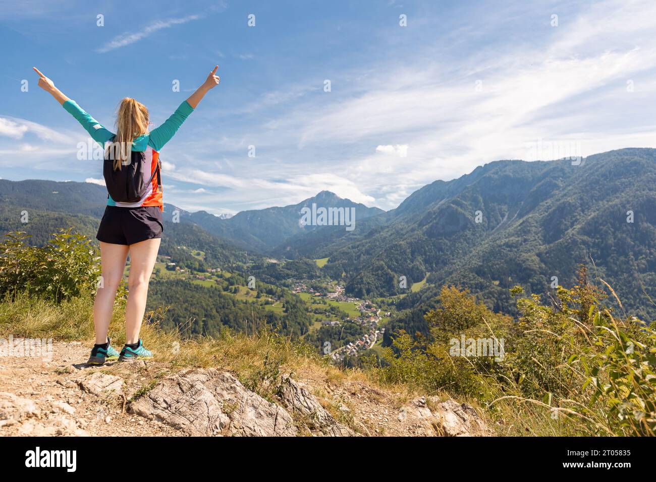 Cheerful girl hiker celebrating her success with raised outstretched arms, enjoying mountain scenery in the summer season. Challenge, goal, and Stock Photo
