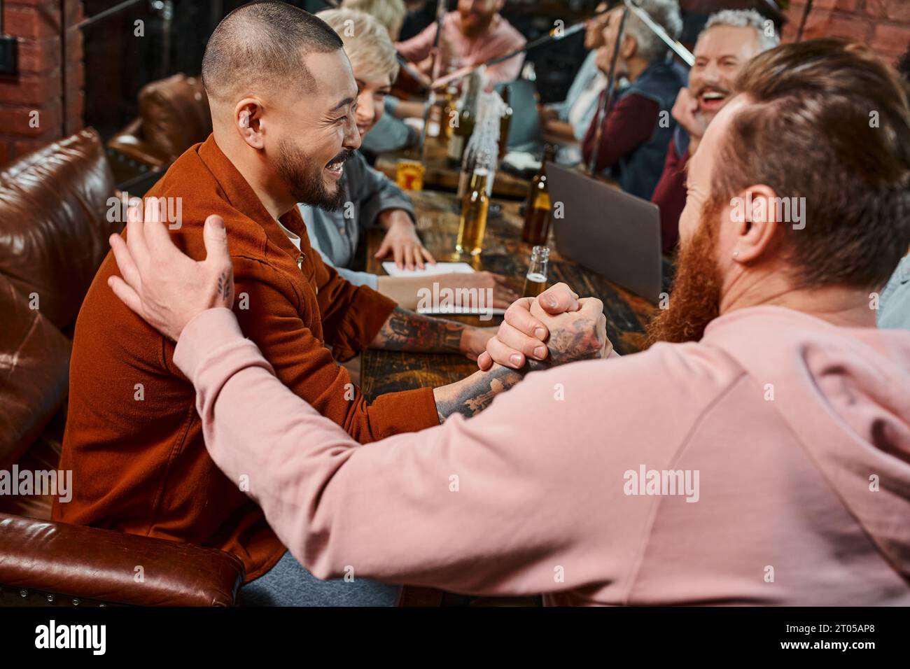 happy multicultural workmates shaking hands near colleagues while spending time in pub after work Stock Photo