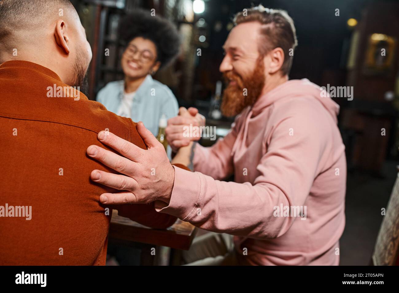 pleased bearded man shaking hands with colleague in pub near blurred african american woman Stock Photo