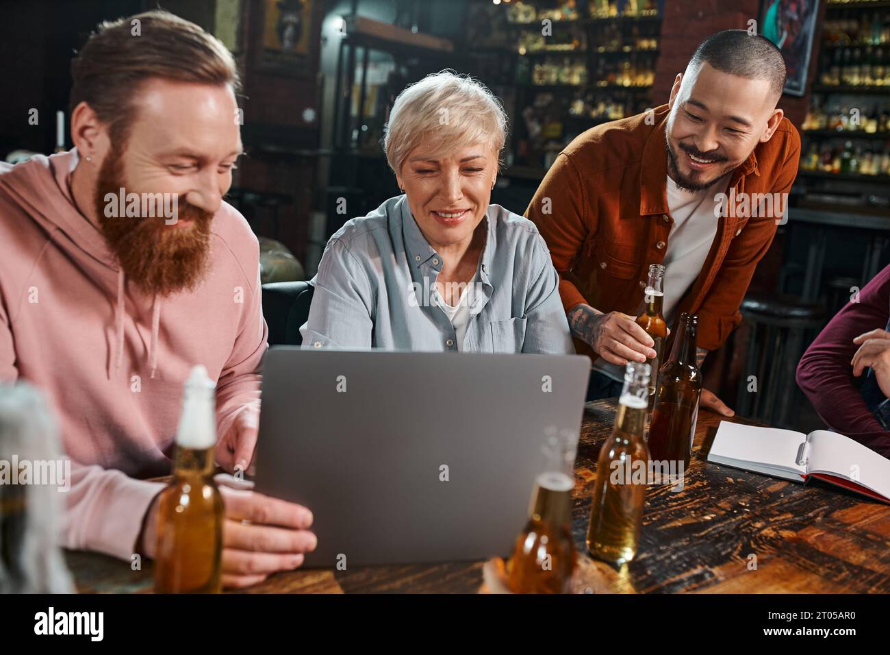 happy multicultural colleagues looking at laptop while sitting with