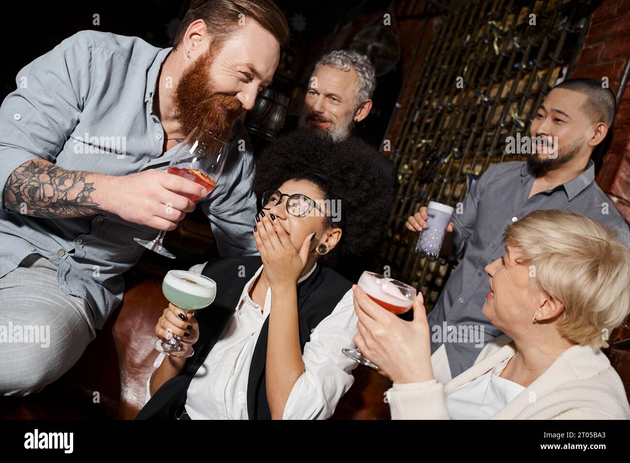 laughing african american woman covering mouth with hand near multiethnic friends with drinks in bar Stock Photo