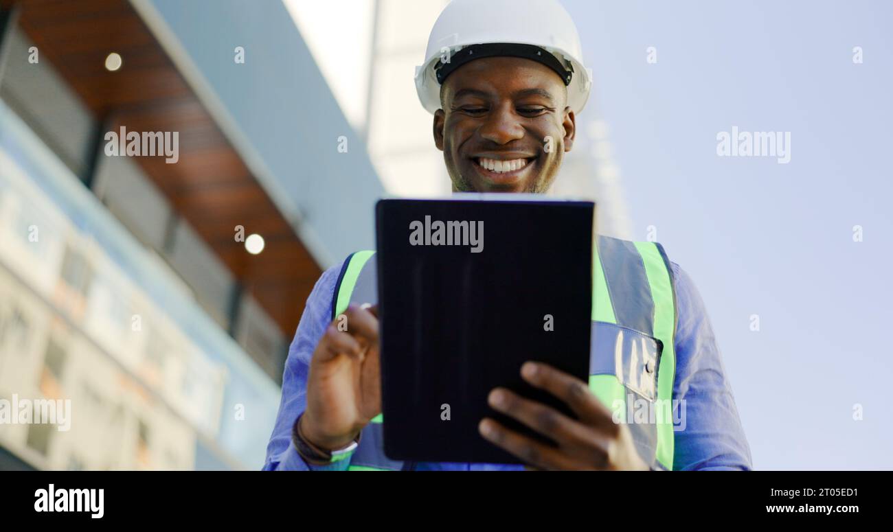 Engineering, man and tablet at construction site inspection, building development and industrial renovation. Excited or happy african worker on Stock Photo