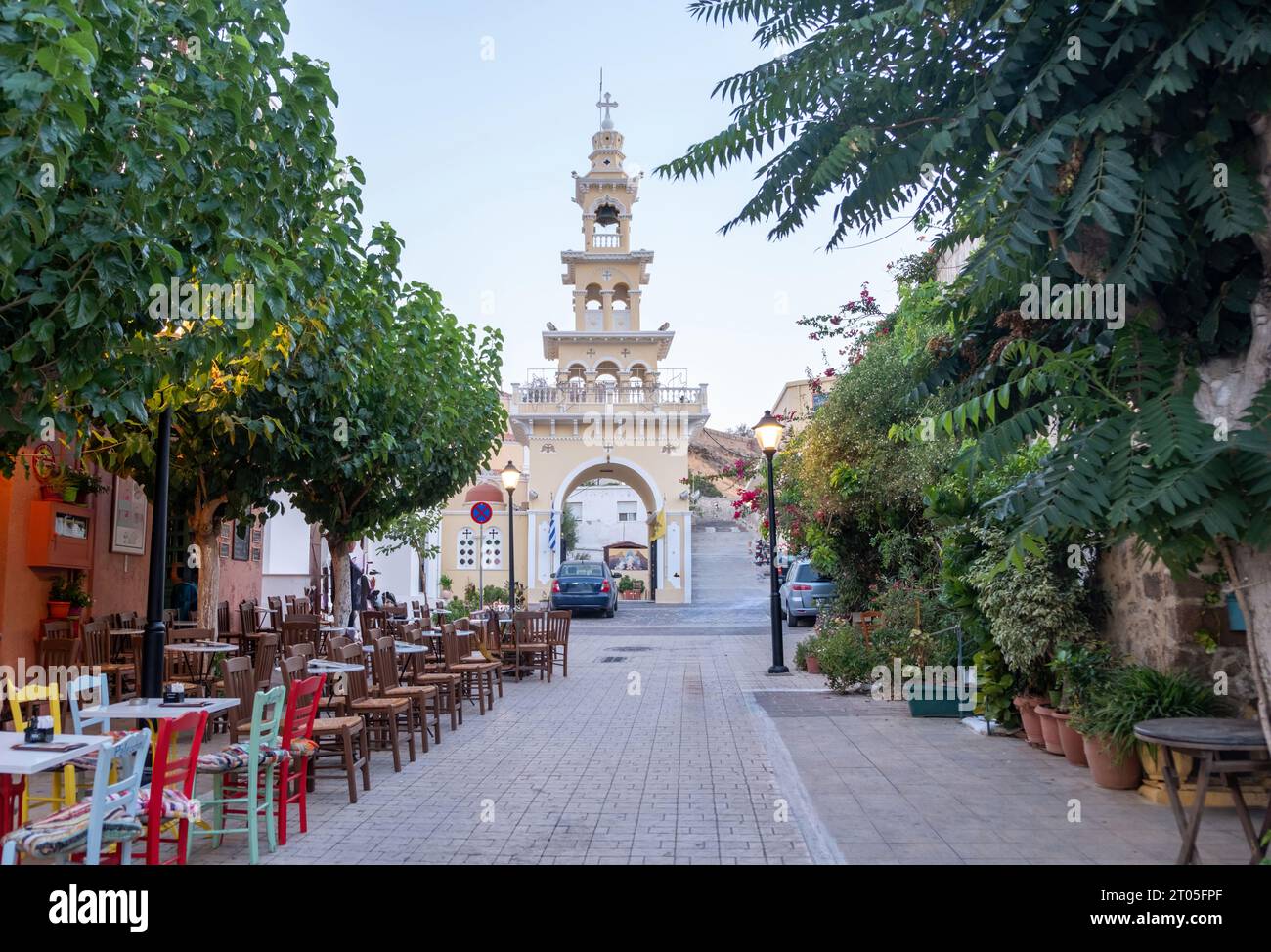 Evangelistra Church Palaiochora Chania, Crete island, Greece. Outdoors cafe on paved street, arched belfry entrance in the afternoon. Stock Photo
