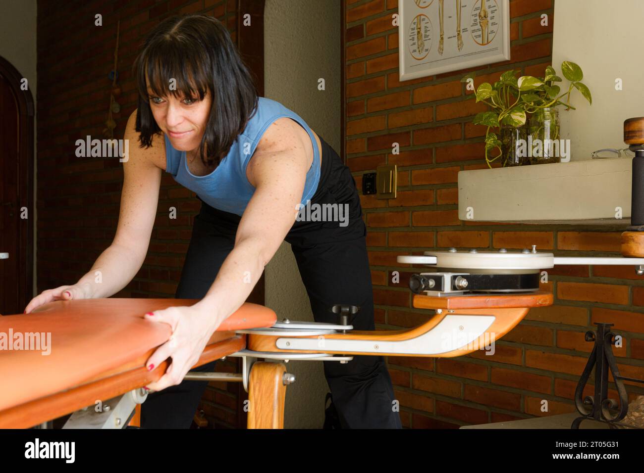 young caucasian woman wall at home positioning and arranging exercise machine training bench at home, preparing to exercise and train. Stock Photo