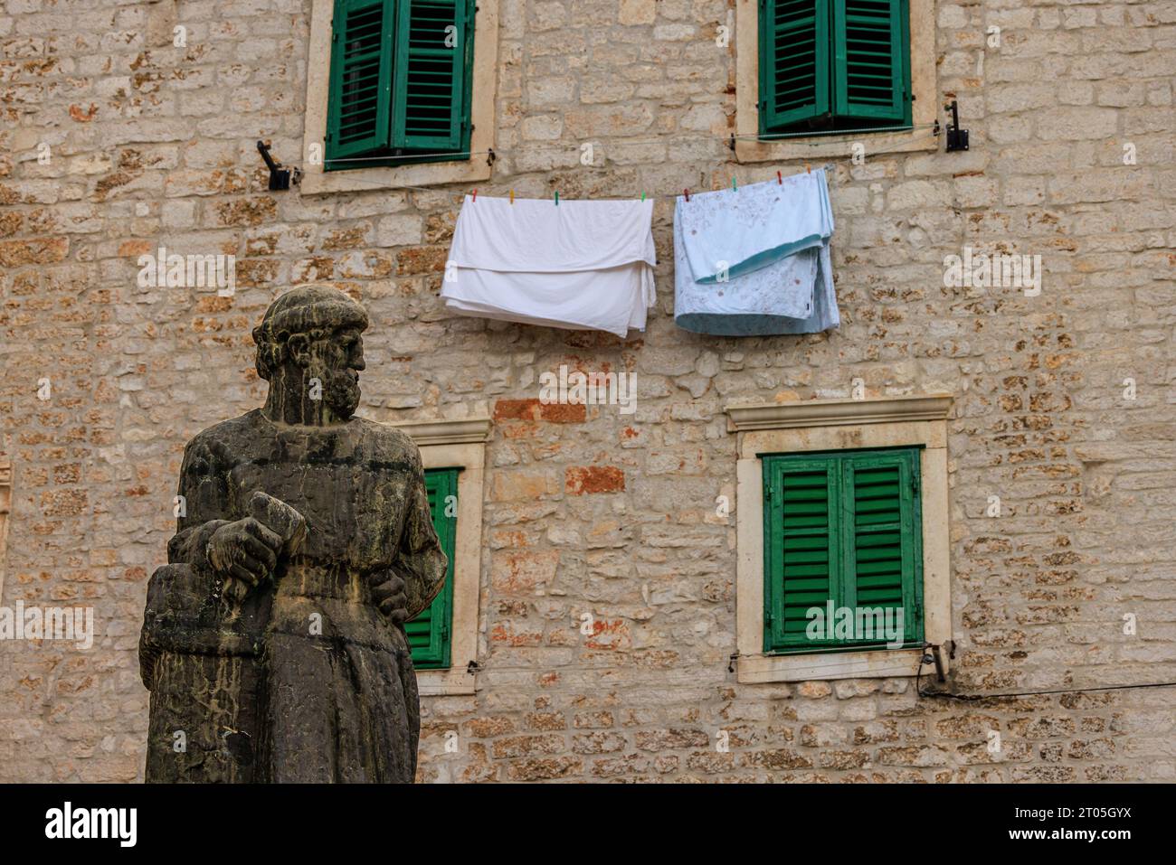 the statue of jurai dalmatinek looks in disdain at clothes hanging out to dry beneath two green shuttered windows in cathedral square sibenik croatia Stock Photo