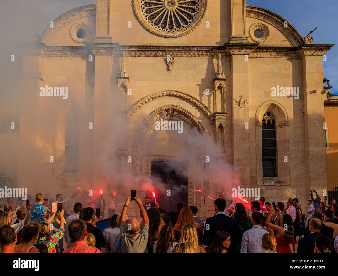 smoke fills the air from red flares as a wedding party celebrates in the early evening sun in front of sibenik cathedral Stock Photo