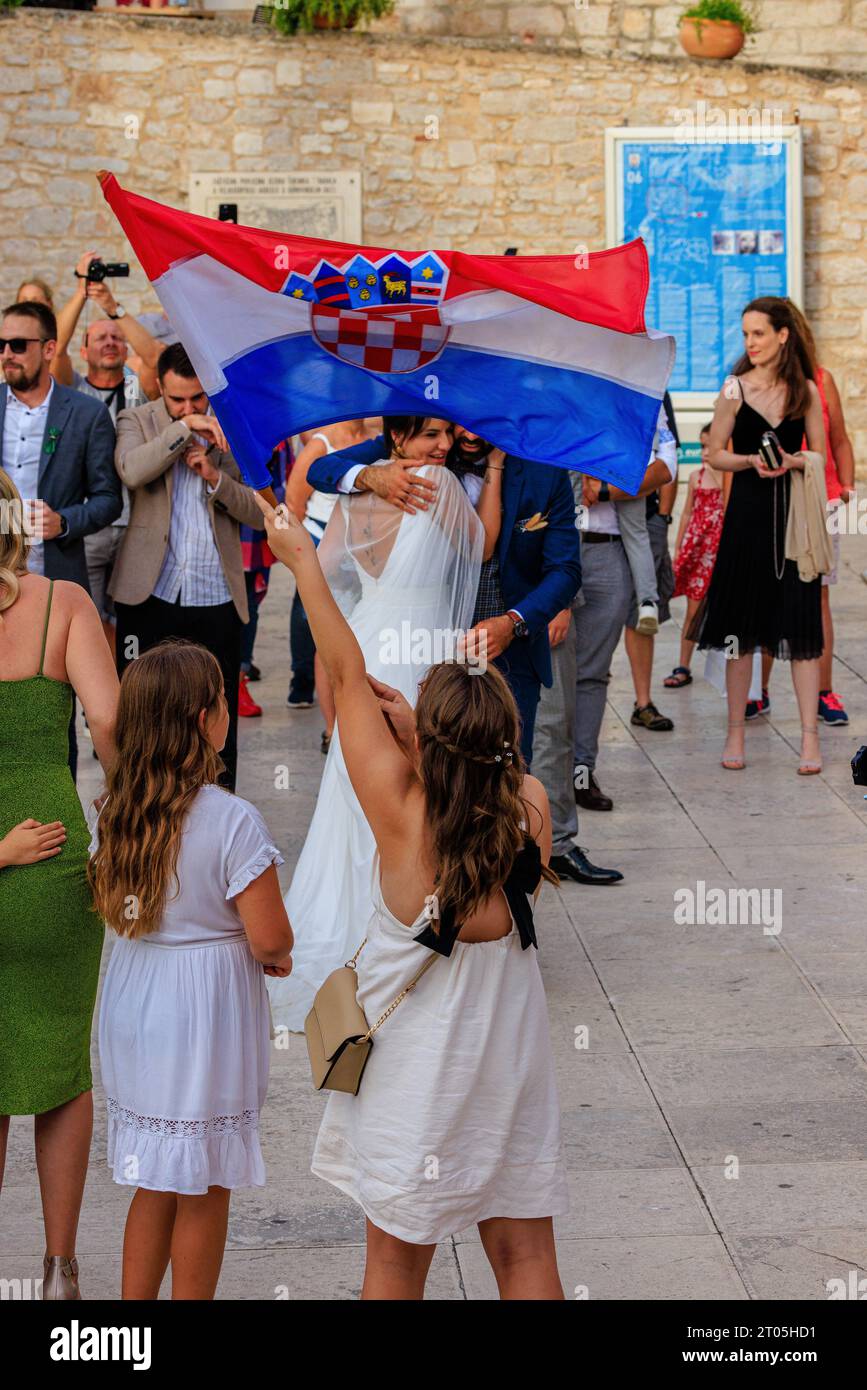 a young girl waves the croatian flag as a bride in white wedding dress hugs and celebrates in the cathedral square in sibenik croatia Stock Photo