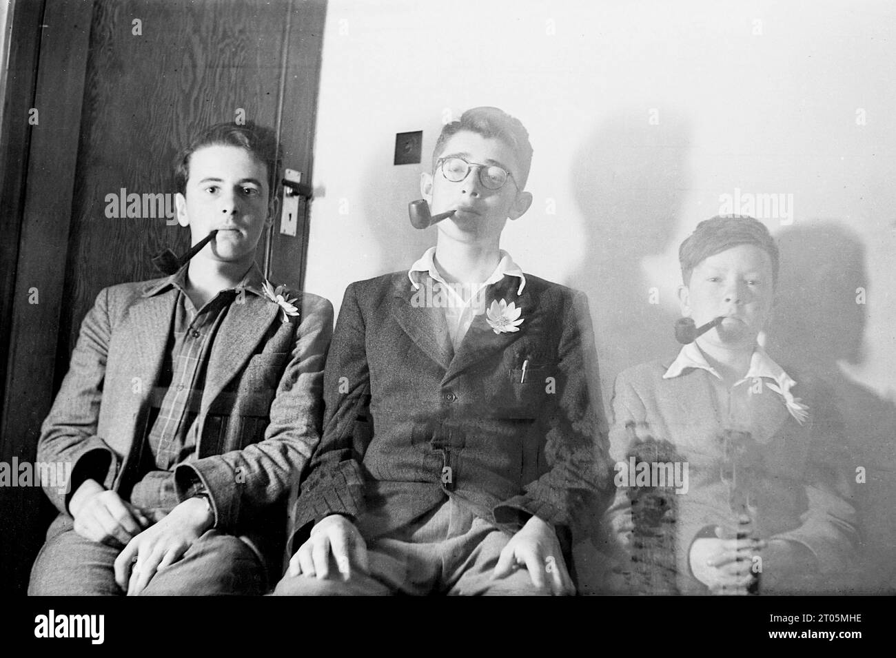 1950s, historical, a young man and two boys all with tobacco pipes in mouths sitting for a fun photo, but light has got into the lens and so we see 'ghosting' on the right of the picture. Stock Photo