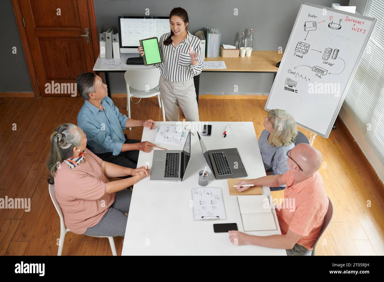 Young woman showing tablet computer with green screen to seniors in computer class Stock Photo