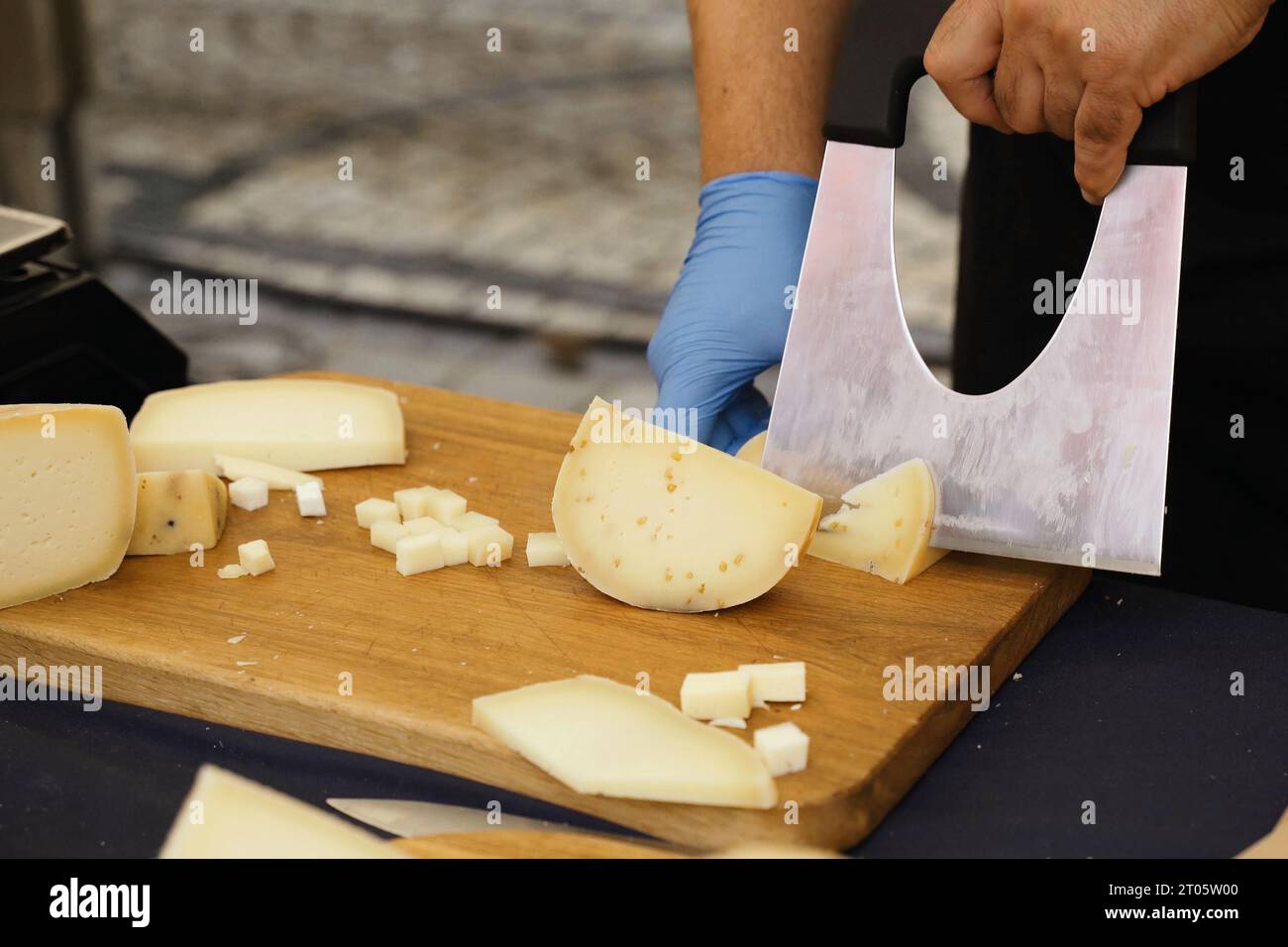 The seller in blue gloves cuts cheese for tasting. Closeup Stock Photo